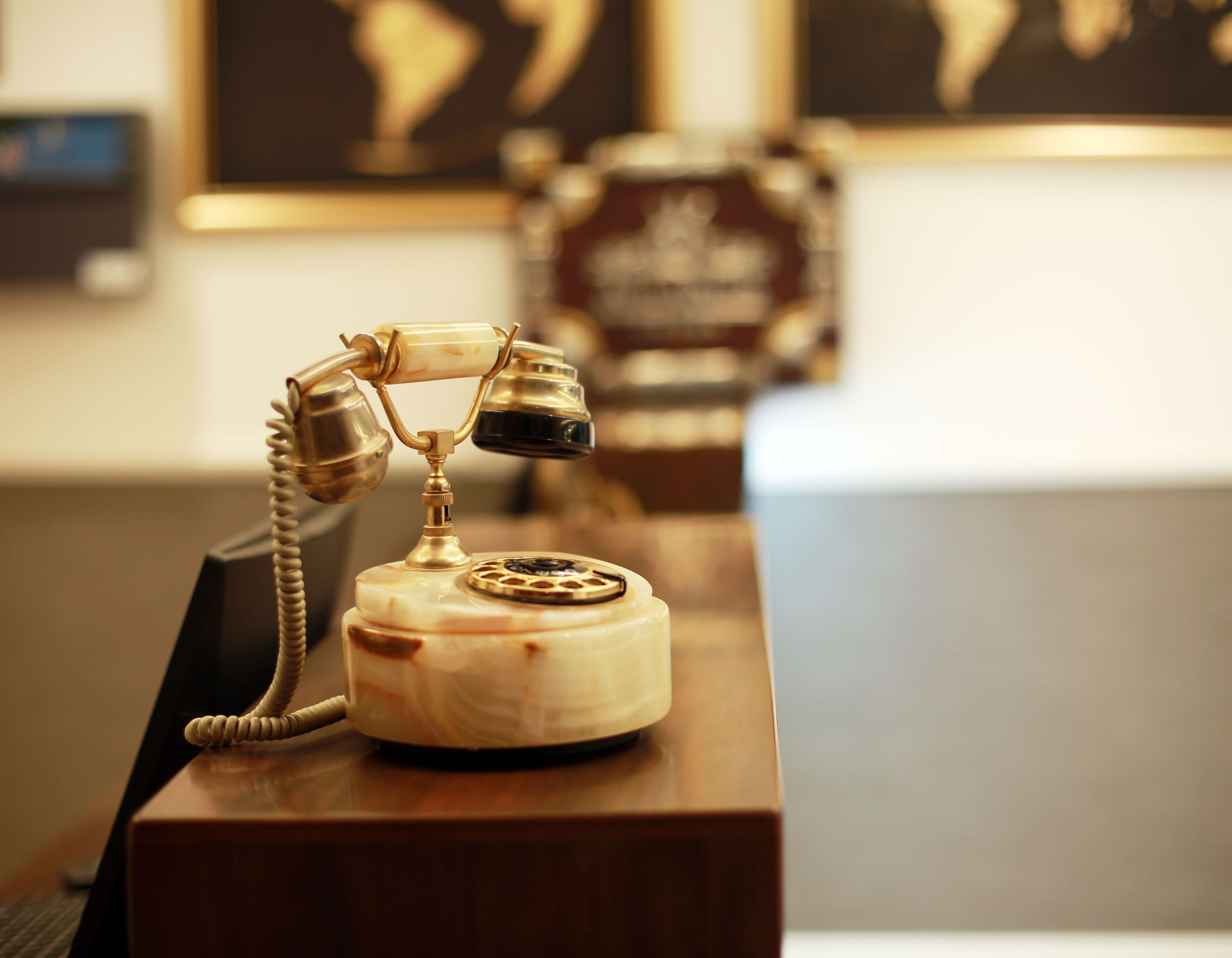 A vintage rotary dial telephone on a wooden desk in a room with a blurred background.