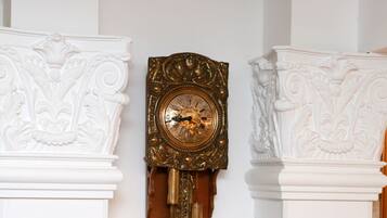 Une horloge ancienne fixée au mur, dotée d’un pendule, et placée entre deux colonnes blanches richement décorées.