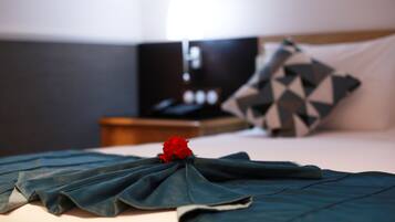 A neatly made bed with a dark blue bedspread, a red rose, and a geometric patterned pillow.