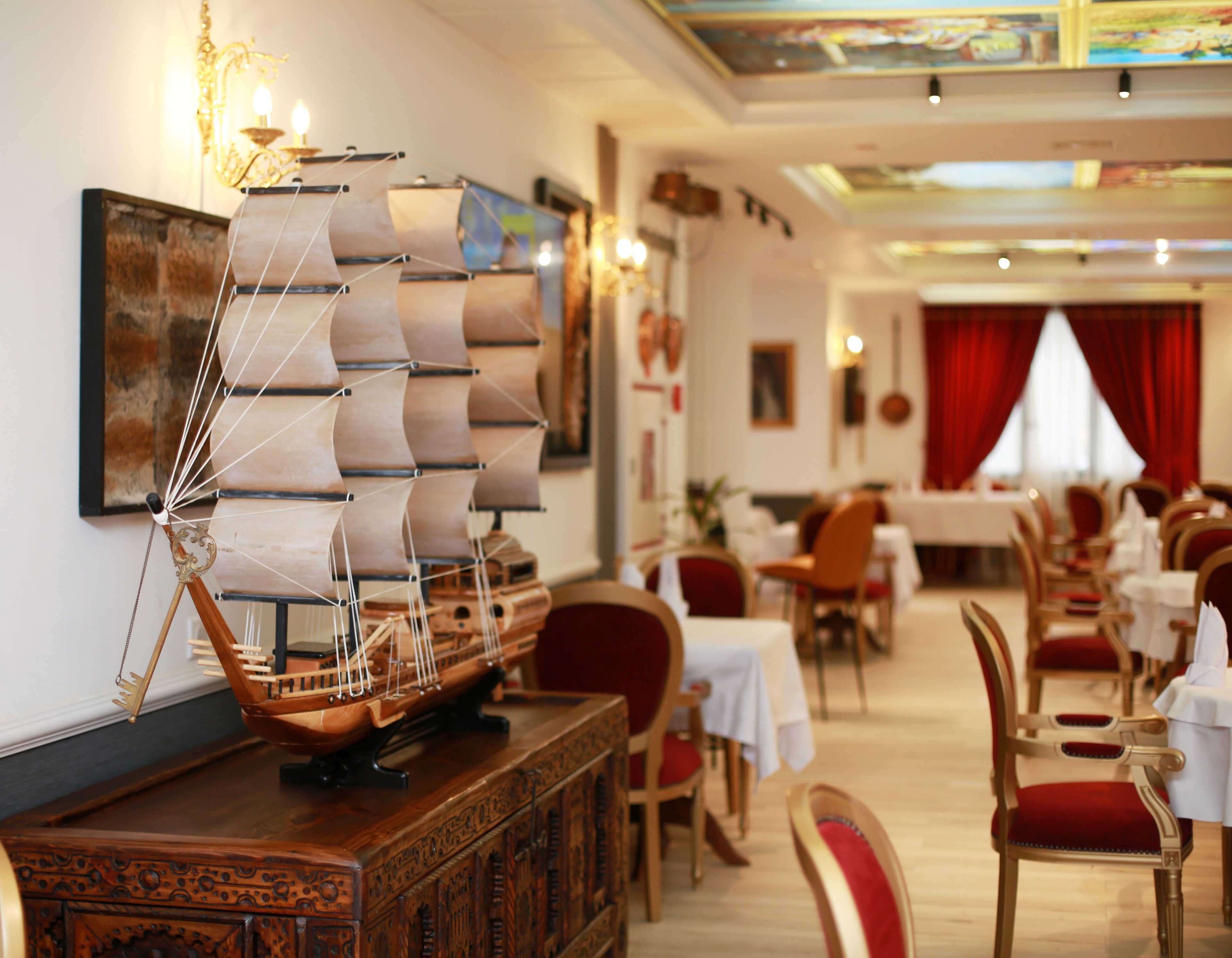 A dining area with tables and chairs, a ship model on a wooden cabinet, and a painting on the wall.
