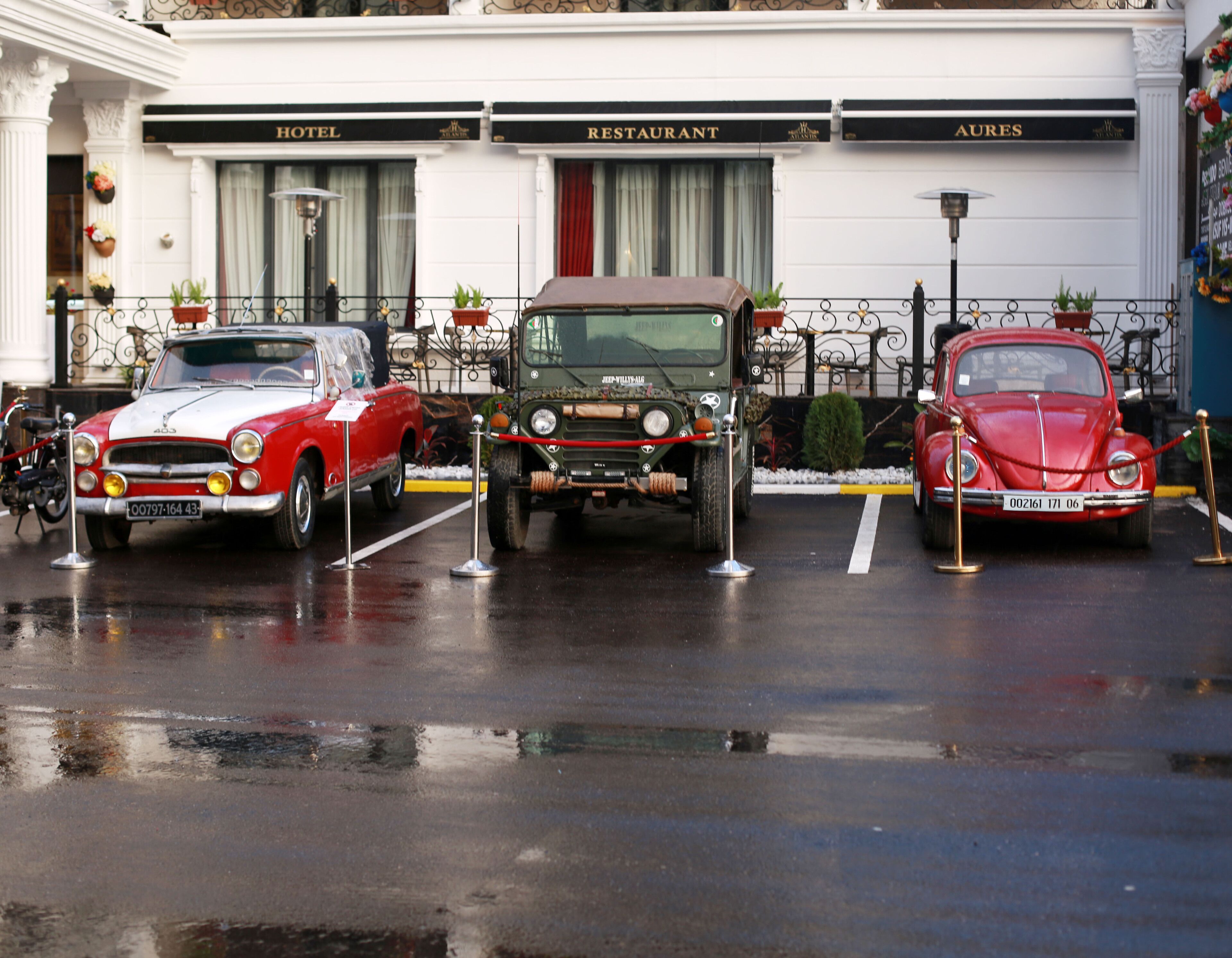 Three vintage cars parked in front of a building with signs for a hotel, restaurant, and a bar.