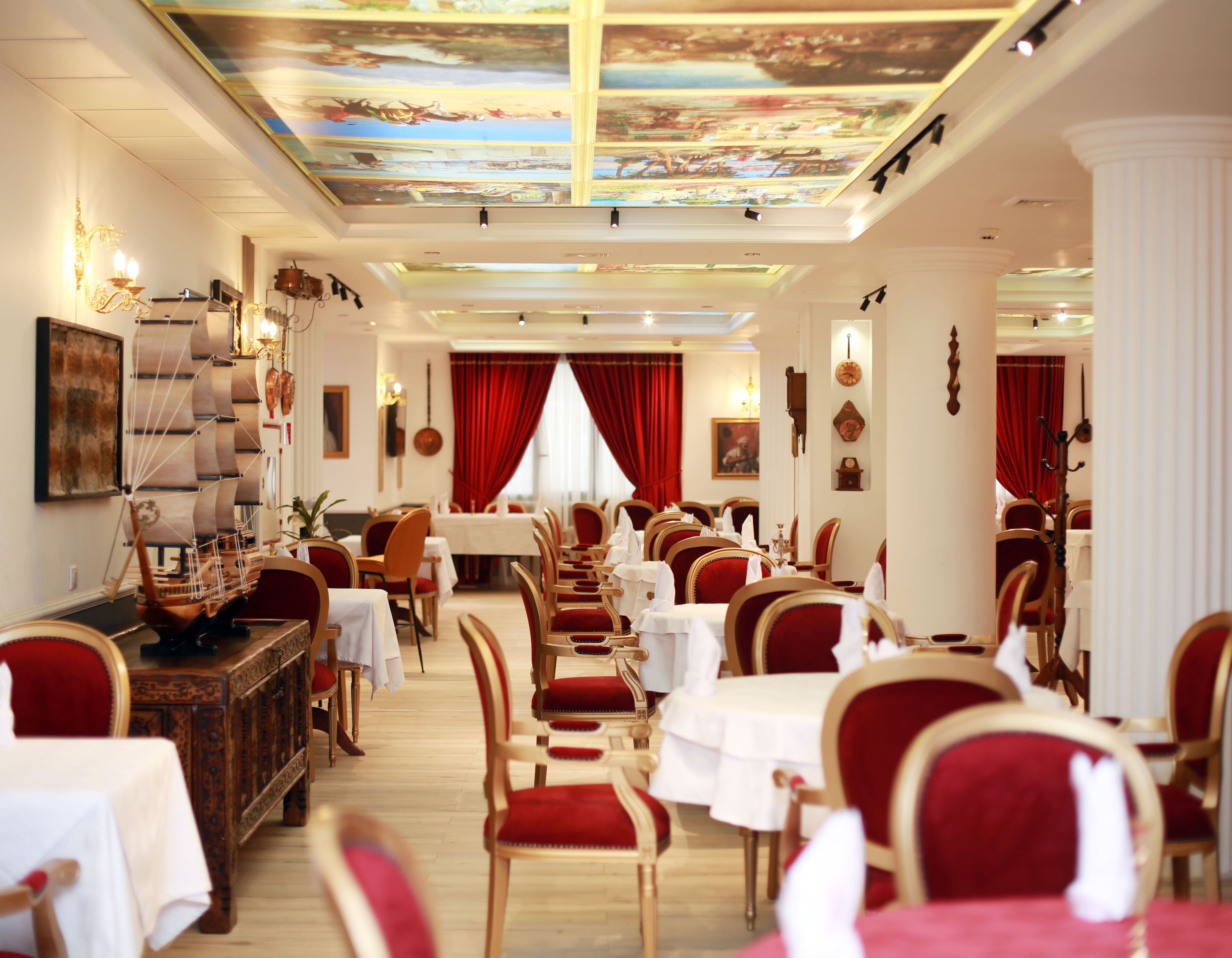 Un comedor formal con varias mesas y sillas, un techo decorativo y cortinas rojas.