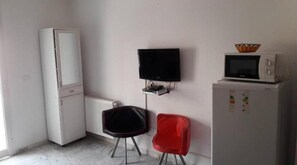 Compact room with a minimalist design, featuring a refrigerator, flat-screen TV, and microwave oven.