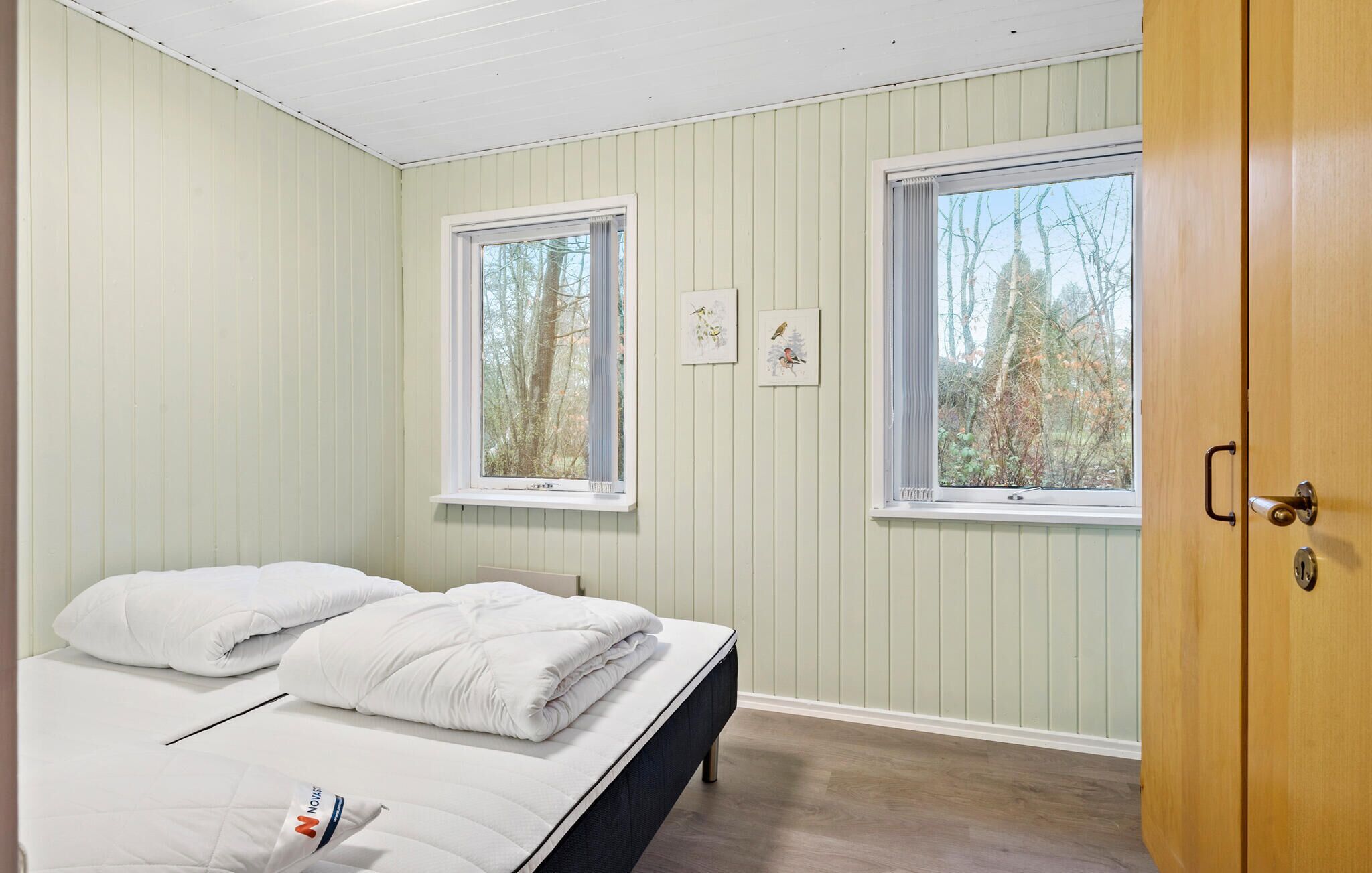 A bedroom with two windows, a bed with white bedding, and a wooden door.