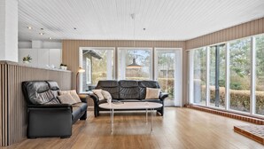 Ein modernes Wohnzimmer mit einer schwarzen Ledersofa-Garnitur, einem Couchtisch und großen Fenstern mit Blick ins Freie.