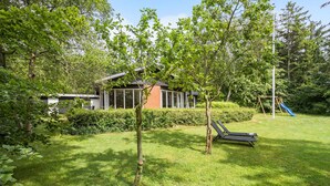 Ein modernes Haus mit Wintergarten, umgeben von üppigem Grün und einem Spielbereich für Kinder mit einer Rutsche.