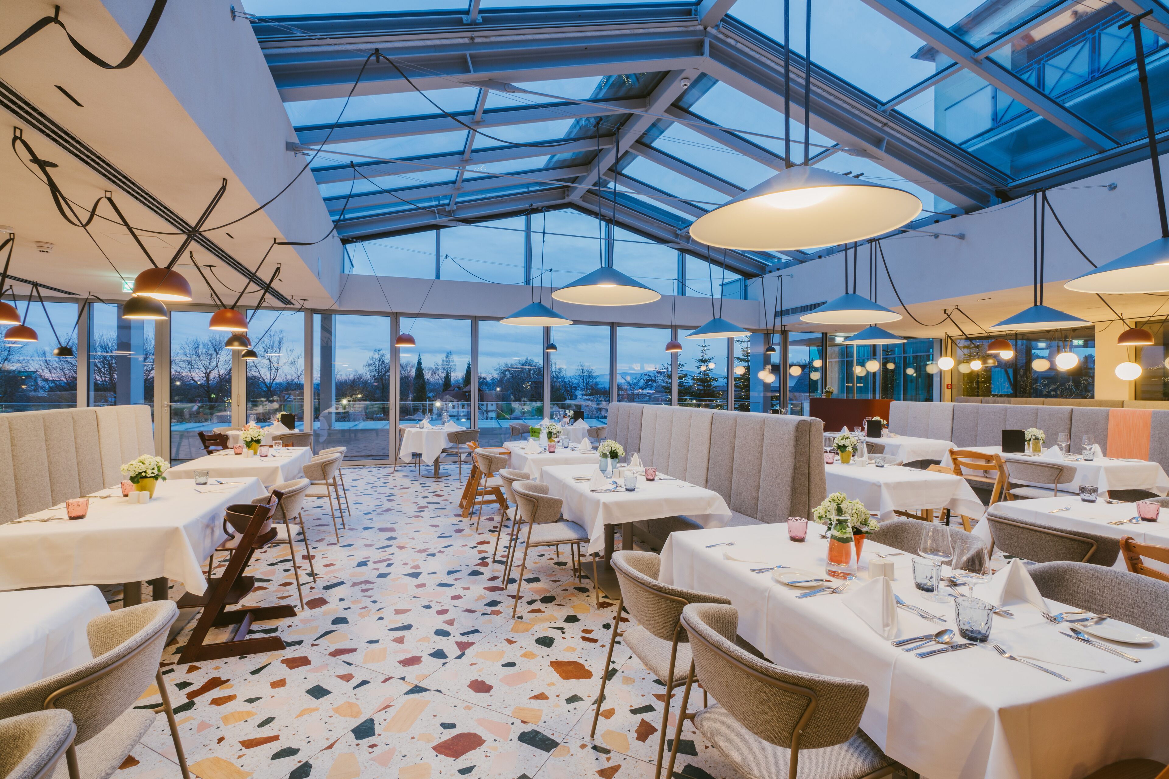 A restaurant with a modern interior, featuring a glass ceiling, white tables, and chairs.