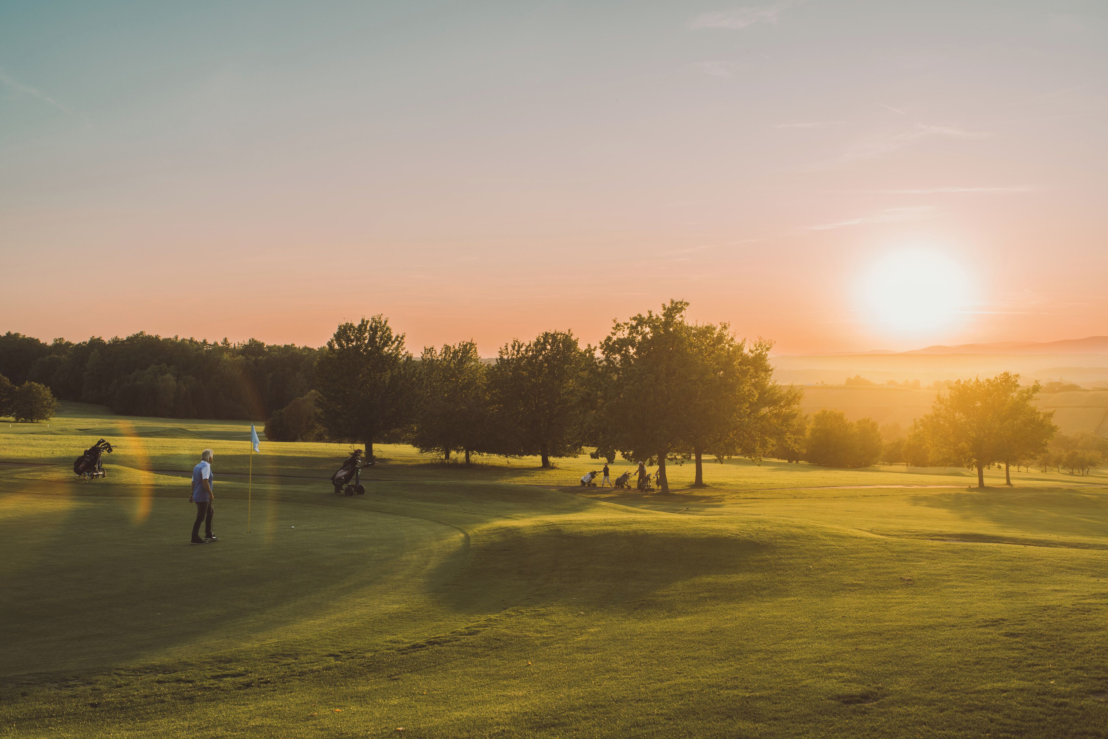 Ein Golfplatz bei Sonnenuntergang, mit Spielern und einer Fahne.