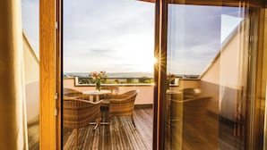 A wooden deck with wicker furniture and a table, overlooking a scenic landscape. - Reiters Finest Family 4s (Bad Tatzmannsdorf)