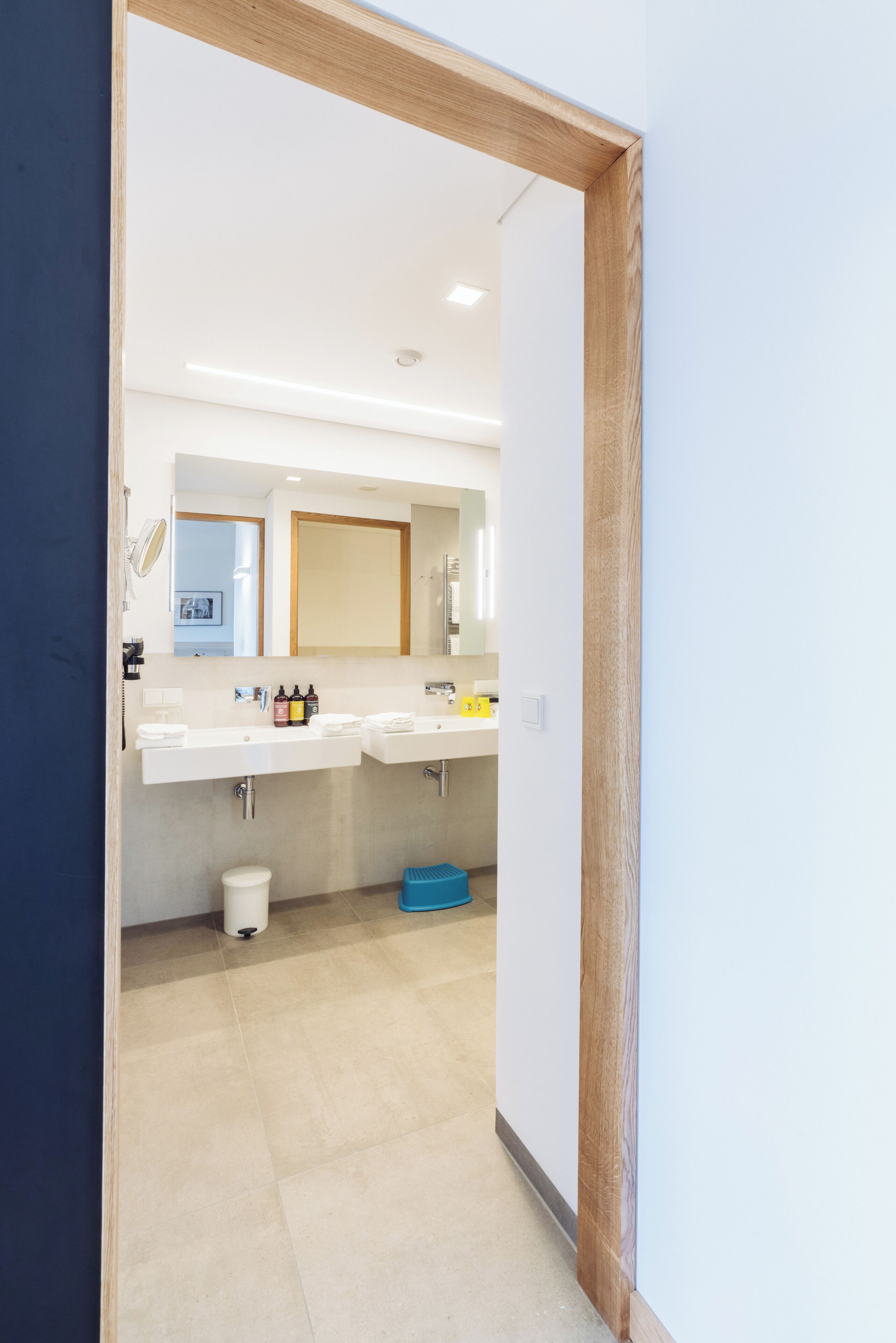 A modern bathroom with two sinks, a mirror, and a blue trash bin.