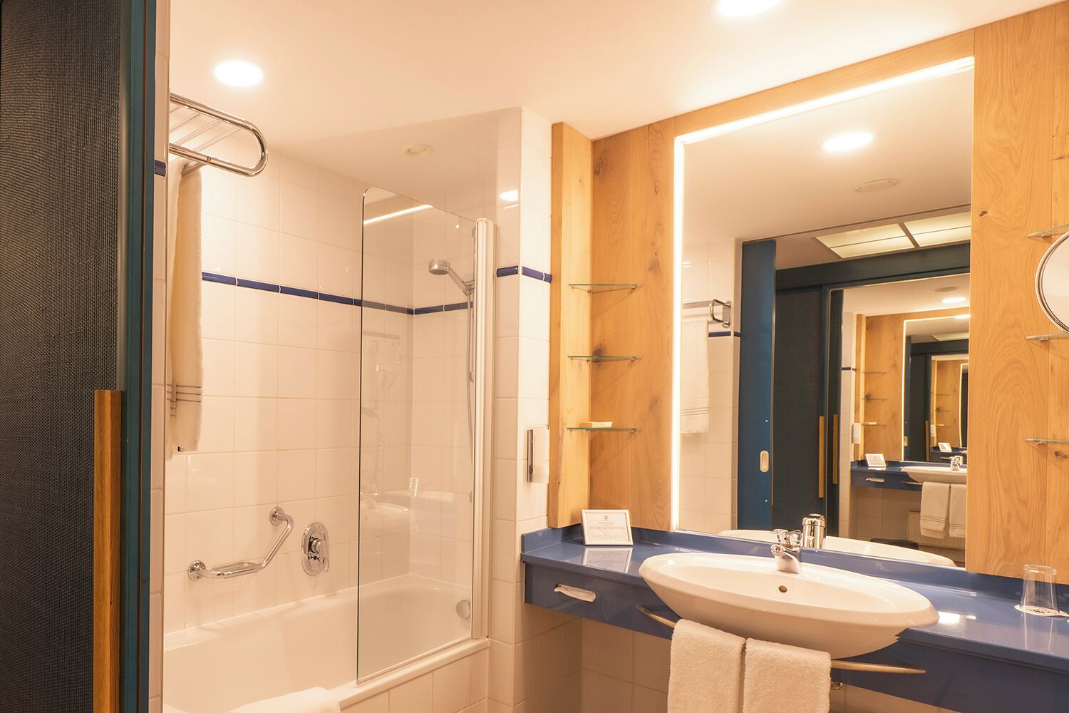 Une salle de bain moderne dotée d’une douche à parois de verre, d’un grand miroir et d’un lavabo sur lequel est posée une serviette.