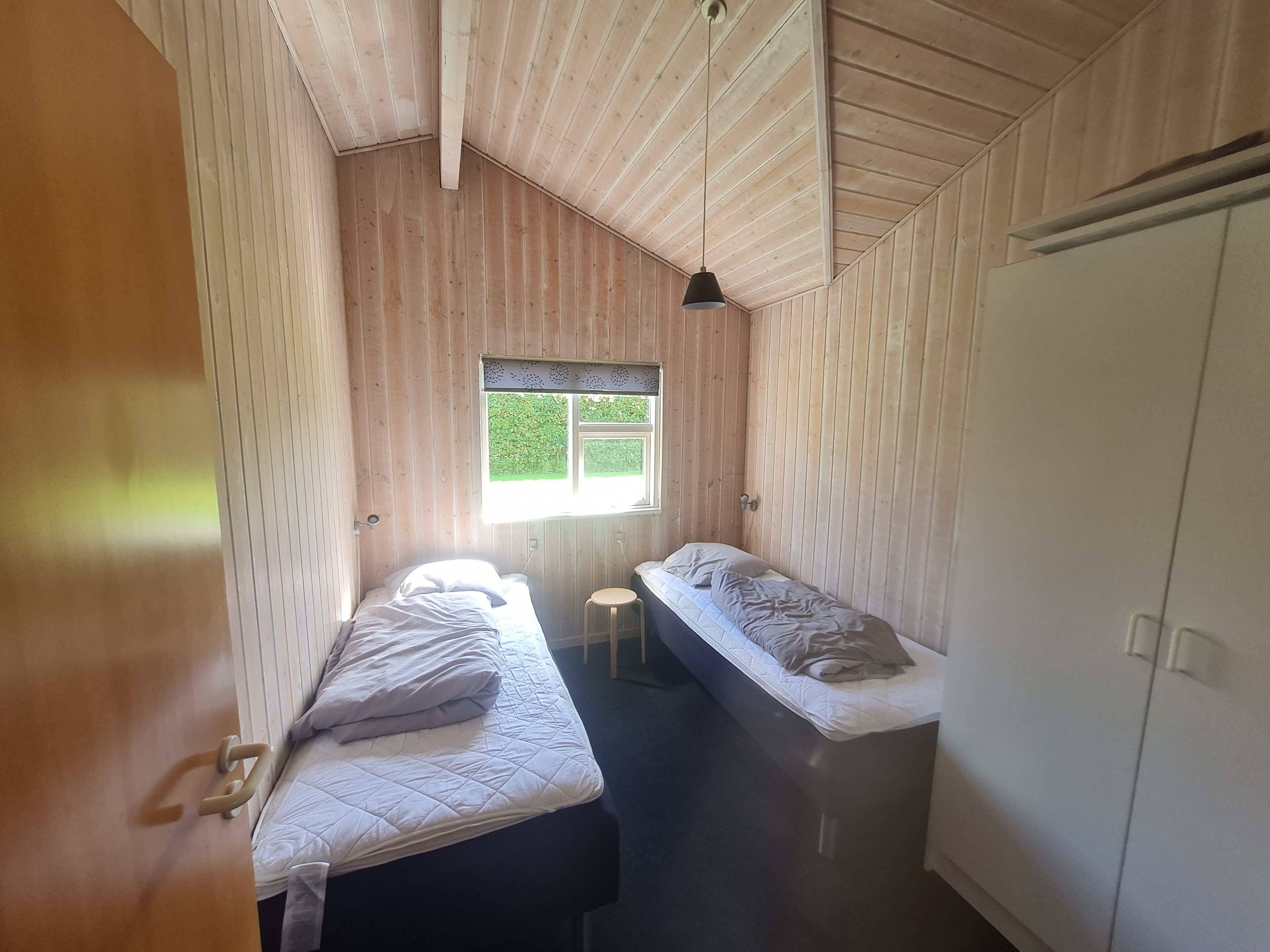 Een kleine, smalle kamer met twee eenpersoonsbedden, een raam en een kledingkast.