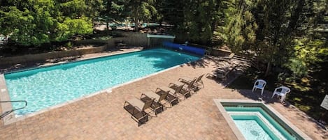 A rectangular swimming pool with a tiled deck, surrounded by trees and shaded by a canopy.
