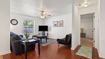 A living room with a ceiling fan, a flat-screen TV, a sofa, a coffee table, and a rug.