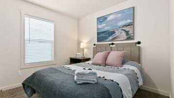 A bedroom with a bed, a nightstand, a lamp, and a painting of a beach scene.