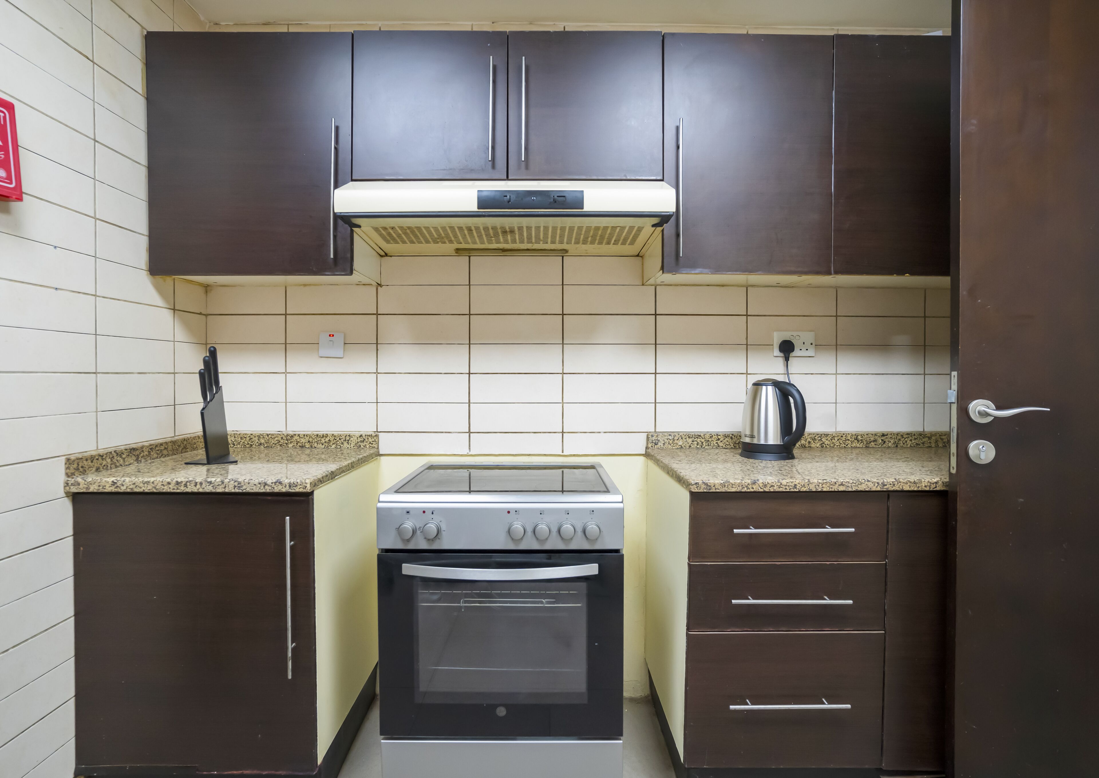 Uma cozinha compacta com armários escuros, fogão a gás, forno, chaleira e bloco de facas.