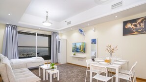 A modern living room with a sofa, dining table, and chairs, a large window with curtains, and artwork on the walls.