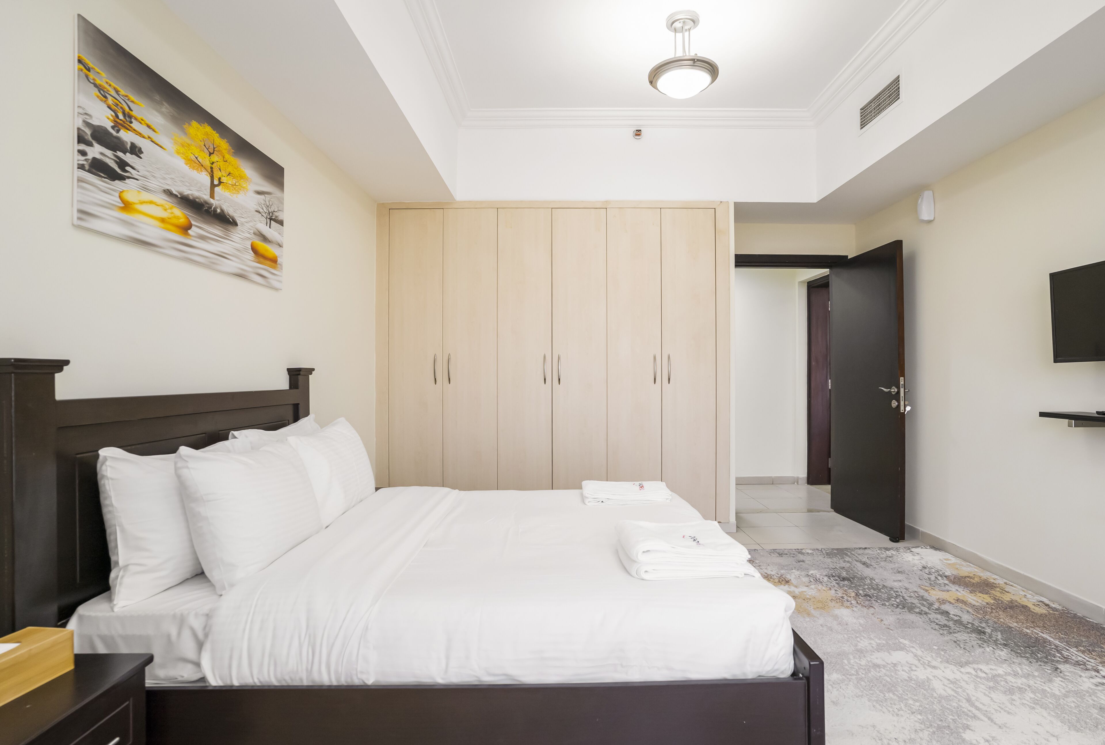 A hotel room with a bed, a wardrobe, a painting, and a TV on the wall.