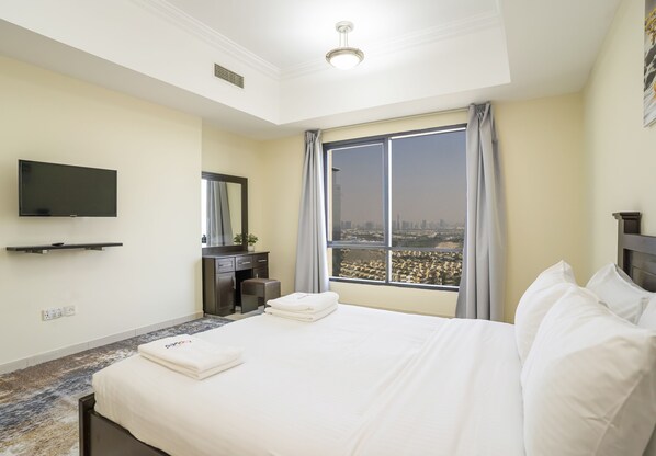 A hotel room with a large bed, a flat-screen TV mounted on the wall, a desk with a chair, and a window with a city view.