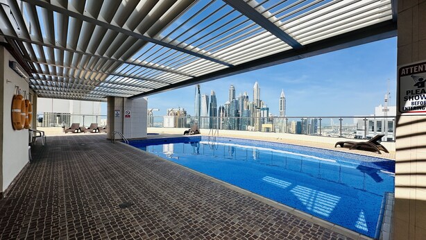 A rooftop pool with a city skyline view, lounge chairs, and a sign indicating a no smoking area.