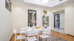 A dining area with a white table set for four, surrounded by white chairs, a vase with flowers, and a mirror on the wall.