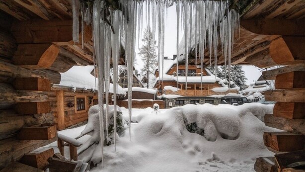 A log cabin with icicles hanging from the ceiling, surrounded by snow-covered ground and a wooden deck. - Mountain Shelter by Loft Affair (Zakopane)