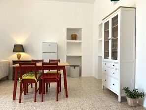 A compact room with a dining table, chairs, a lamp, a white cabinet with glass doors, and a small potted plant.