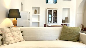 A white sofa with patterned pillows, a table with chairs, a cabinet, and a window with curtains. - La Casedda Verde - Pisticci - nature and relaxation (Basilicata)