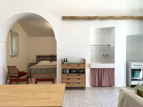 A compact room with a bed, a wooden table, a kitchenette, and a small seating area.