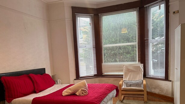 A bedroom with a bed, a chair, and large windows. - Balham Double Deluxe Room 1 (London)