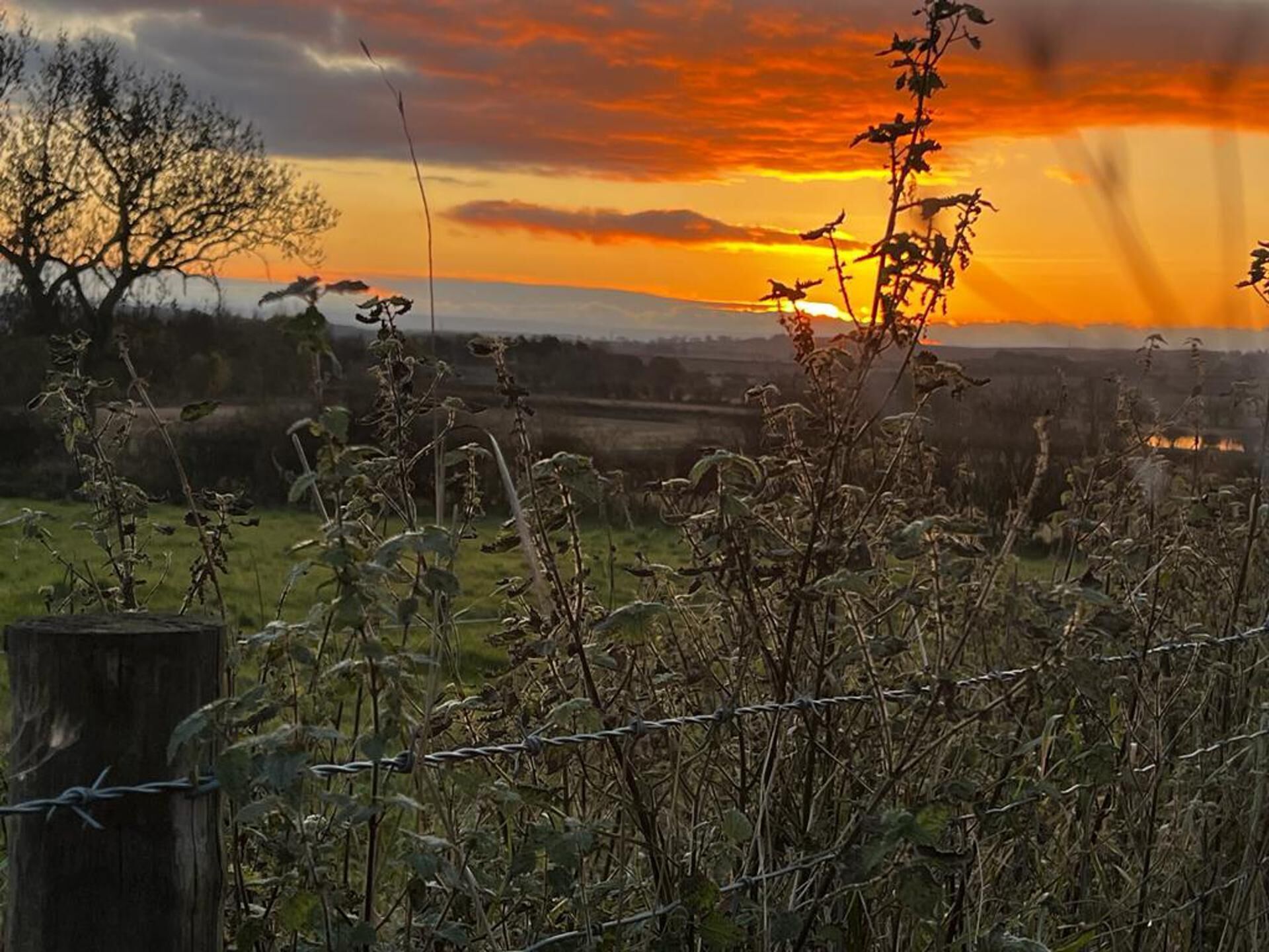 A sunset over a rural landscape with a barbed wire fence in the foreground.
