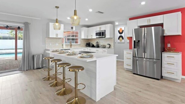 Una cocina moderna con armarios blancos, un refrigerador de acero inoxidable grande y una isla central con taburetes.