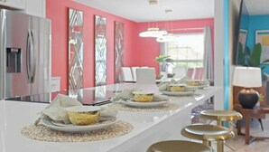 Una cocina moderna con una isla blanca, paredes rosas y electrodomésticos de acero inoxidable.