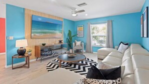 Una sala de estar moderna con una pared azul, un cuadro grande, un sofá, una mesa de centro y un televisor.