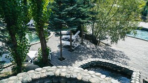 A stone hot tub surrounded by a wooden deck, with lounge chairs and trees in the background. - Mountain View Hot Spring Resort (Koy-Tash)