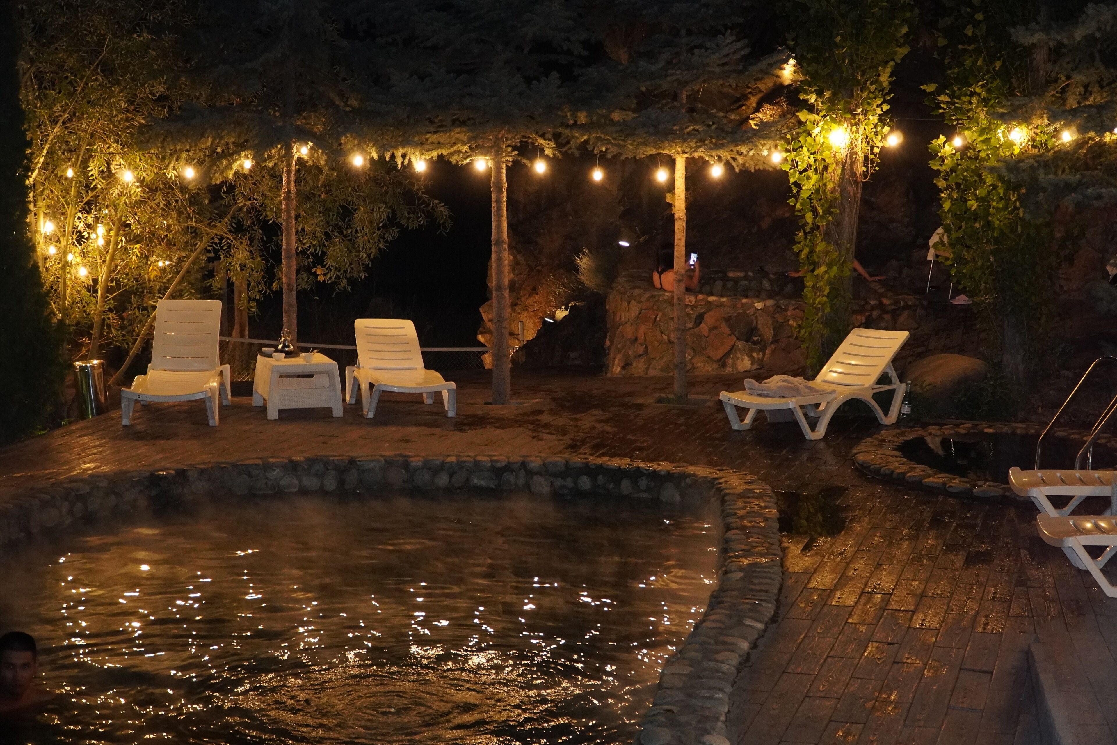 An outdoor pool area with lounge chairs and string lights.