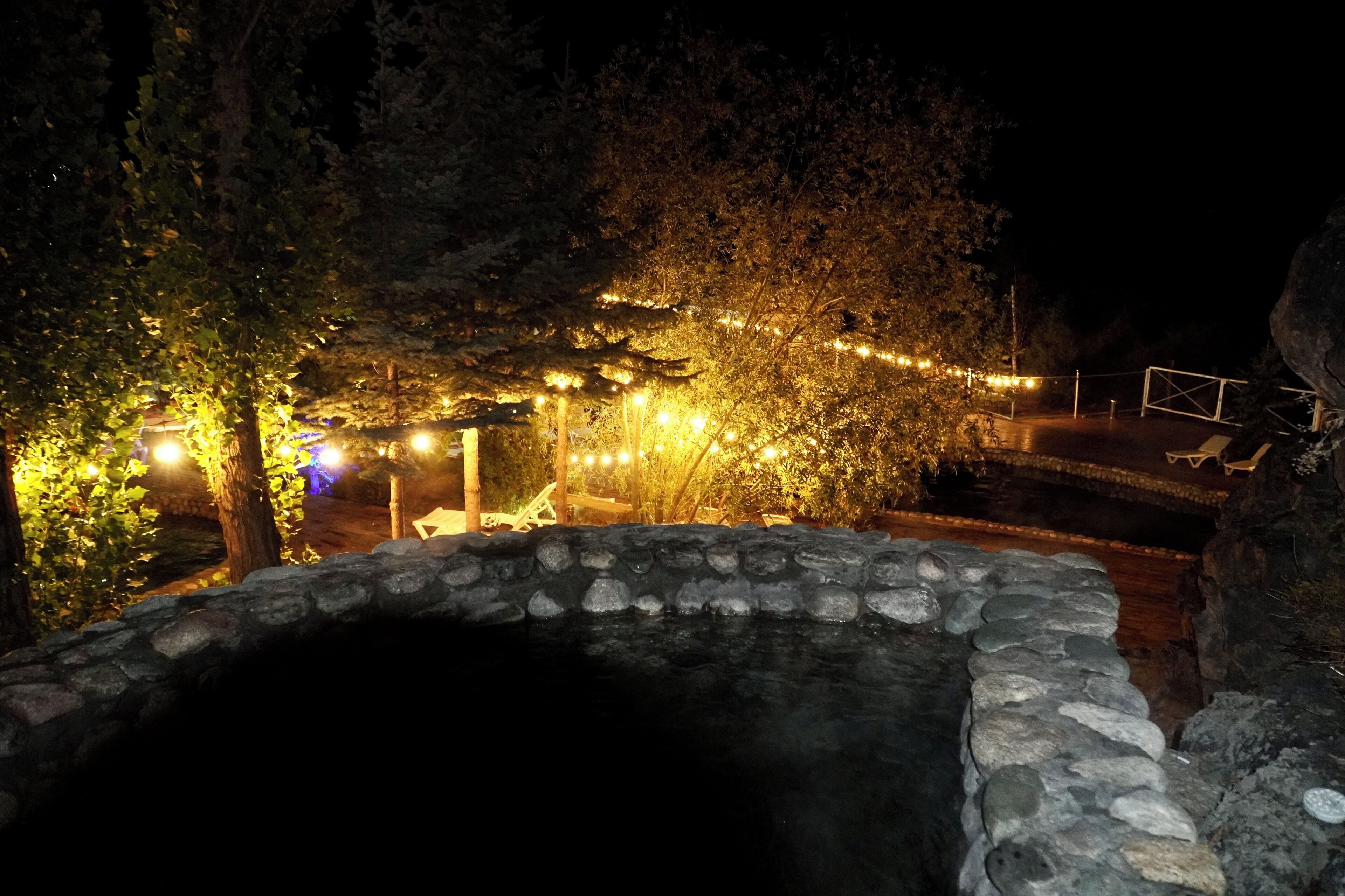 Un pozo de piedra rodeado de árboles e iluminado con luces de cuerda.