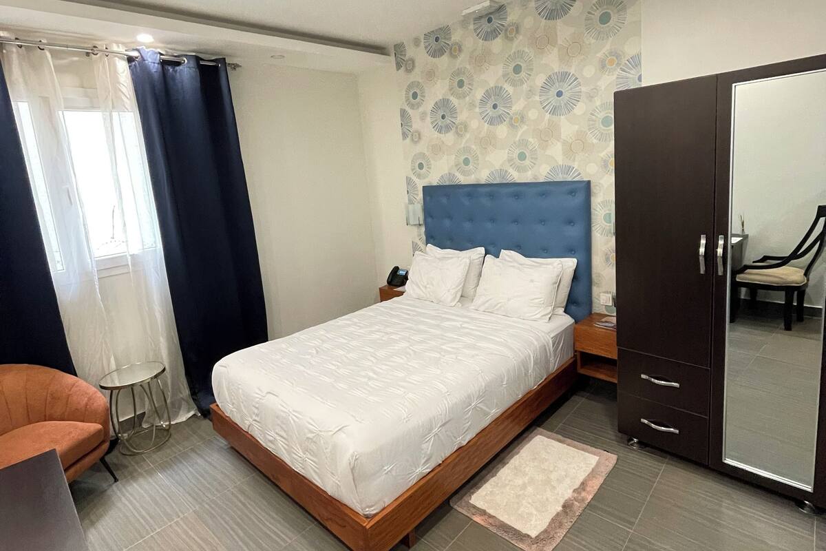 A modern bedroom with a large bed, a wardrobe, a desk, and a chair.