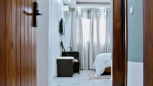 Una moderna camera d'albergo con una porta in legno, un pavimento in marmo, un letto con copriletto bianco, una scrivania con sedia e una TV appesa al muro.