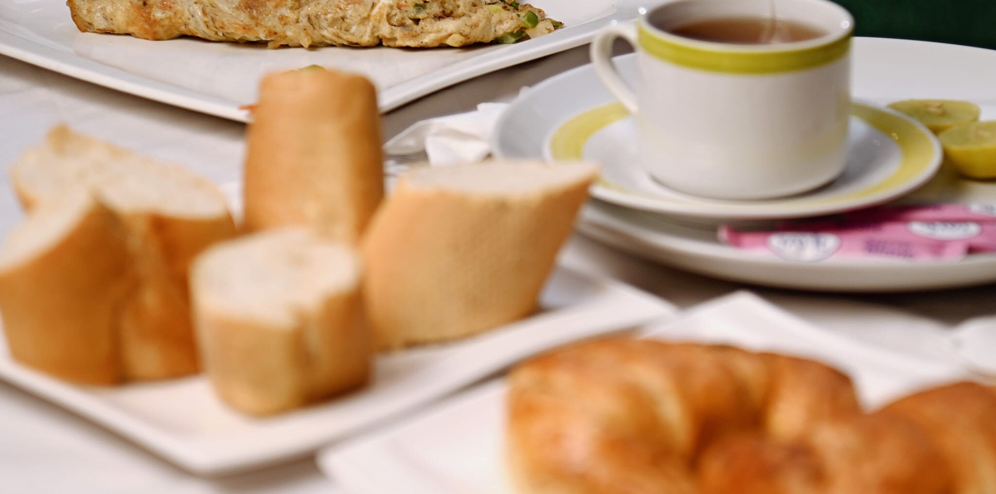 A breakfast setting with bread, a croissant, and a cup of coffee on a plate.