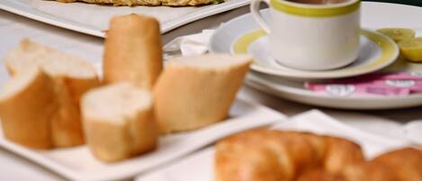 A breakfast setting with bread, a croissant, and a cup of coffee on a plate.