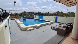 Una piscina sul tetto con solarium piastrellato, poltrone relax e vista sugli edifici circostanti.