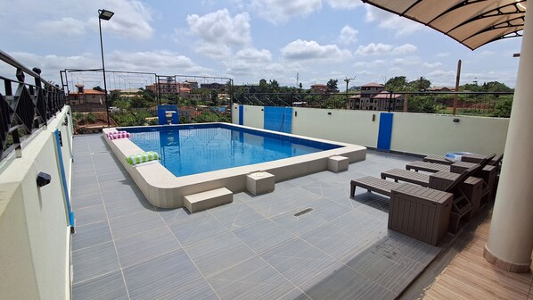 Una piscina en la azotea con solárium de baldosas, sillas de descanso y vistas de los edificios circundantes.