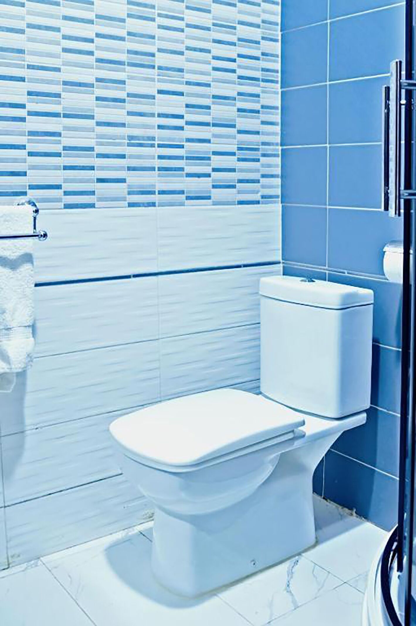 Un bagno con il water bianco, pareti rivestite di piastrelle blu e una finestra con persiane.