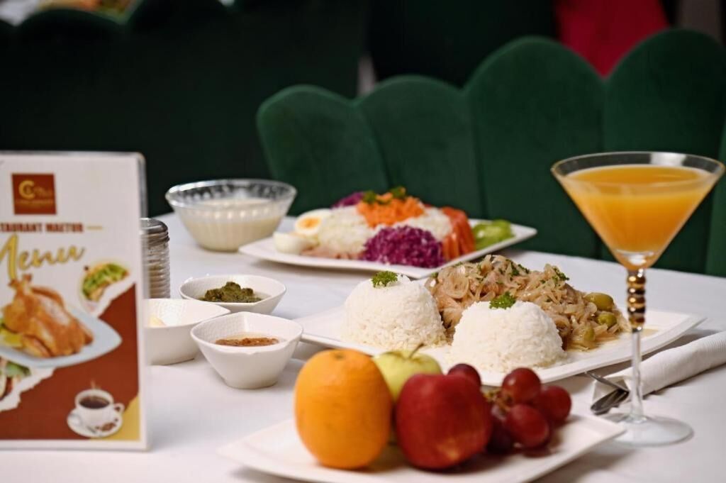 Une table dressée avec une variété de plats, notamment du riz, des légumes et un verre de jus d’orange.