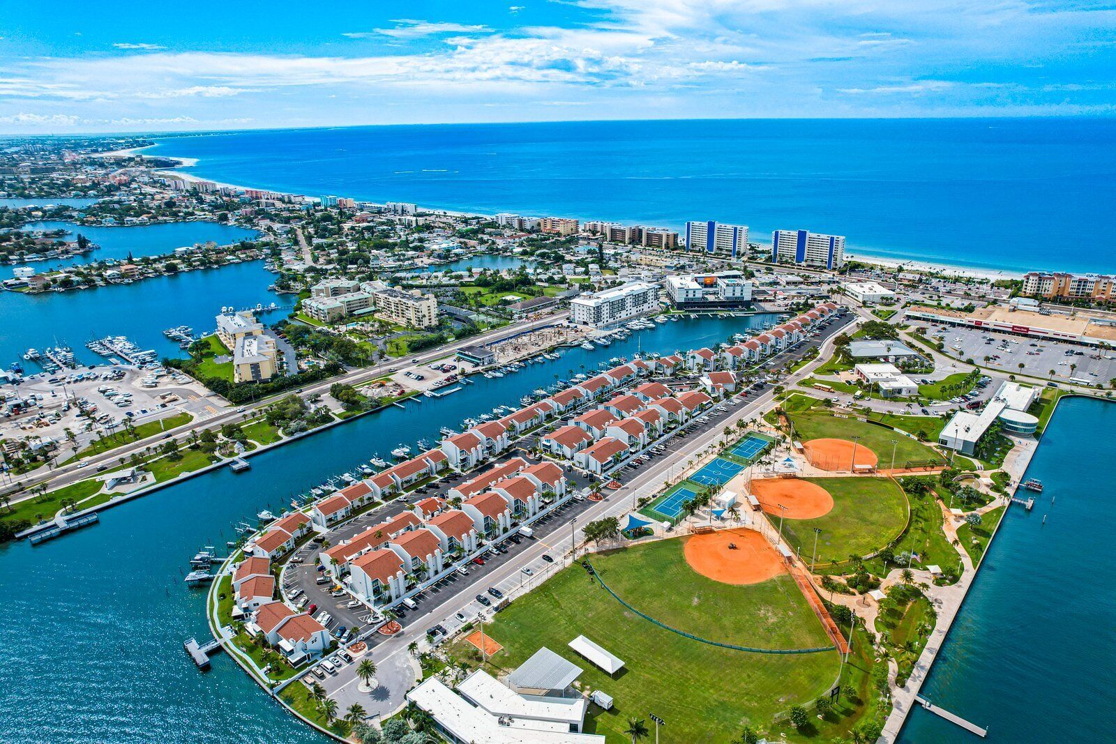 An aerial view of a coastal city with a marina, residential buildings, and sports facilities.