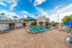 A pool area with lounge chairs, a pool, and a building with a blue roof.