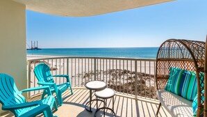 Un balcon avec des chaises turquoise, une petite table et un canapé en osier agrémenté de coussins à rayures, donnant sur une plage et une jetée.