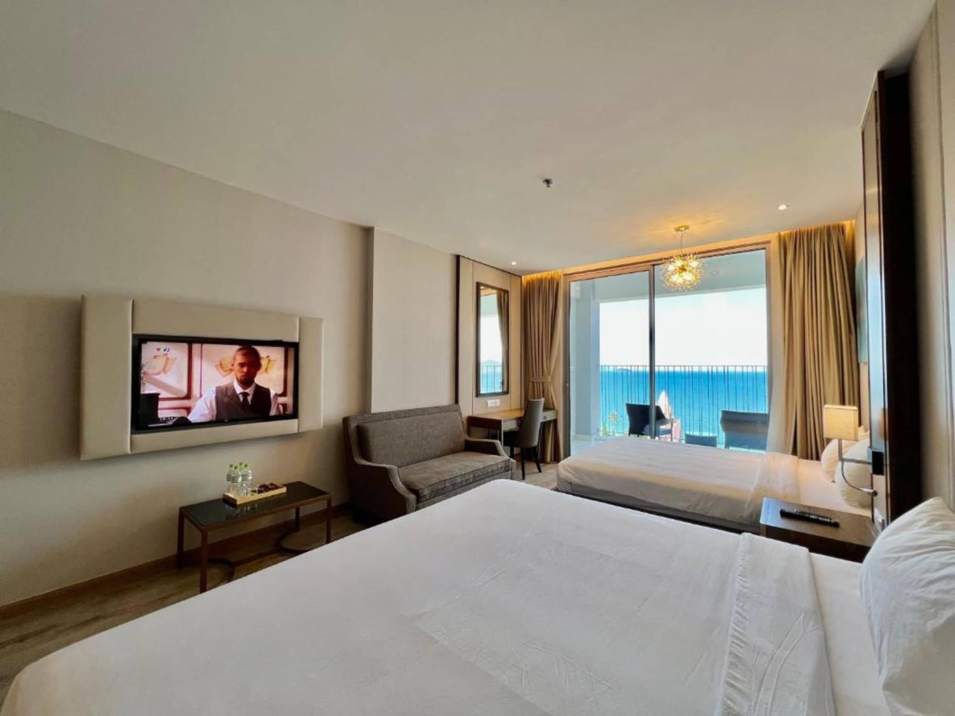 Une chambre d’hôtel avec deux lits, un téléviseur fixé au mur, un bureau avec une chaise et une grande fenêtre donnant sur la mer.