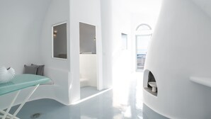 Una habitación moderna y minimalista con techo curvo, una mesa de vidrio y una pequeña zona de estar con cojines.